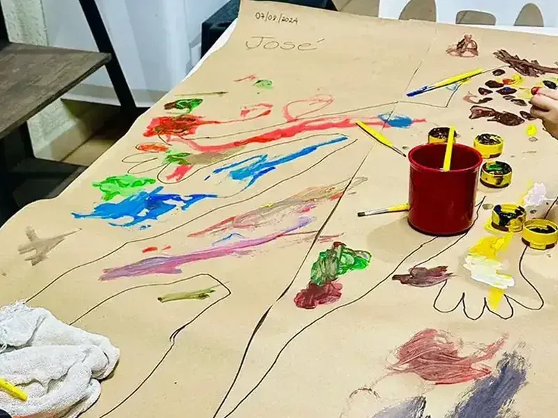 Espaço de recreação e arte do NUAMCE com mesa ampla, tintas e papéis, sem crianças