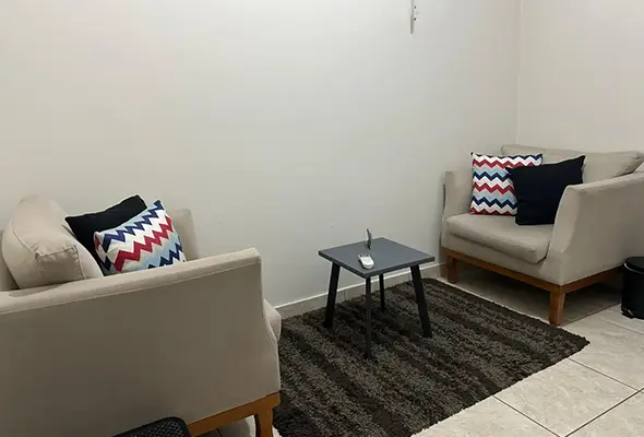 Sala confortável com poltronas claras, almofadas decorativas e mesa de apoio, em ambiente da Clínica de Psicanálise Nuamce em Campinas.