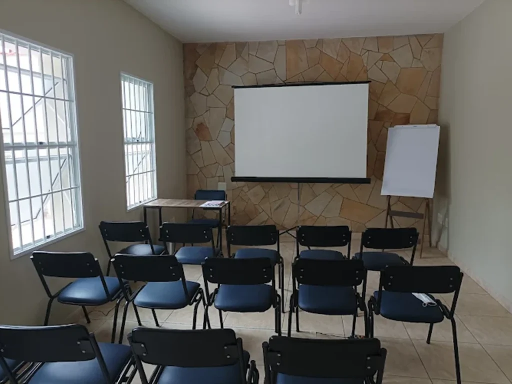 Sala de aula com cadeiras enfileiradas, tela de projeção e flip chart preparados para módulo de formação continuada em psicanálise em Campinas.