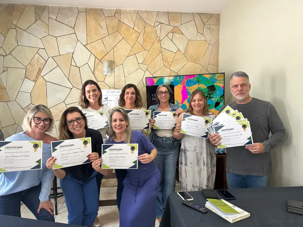 Grupo de alunos e professores sorrindo e exibindo certificados de participação após conclusão de curso de formação continuada em psicanálise na Clínica Nuamce em Campinas.