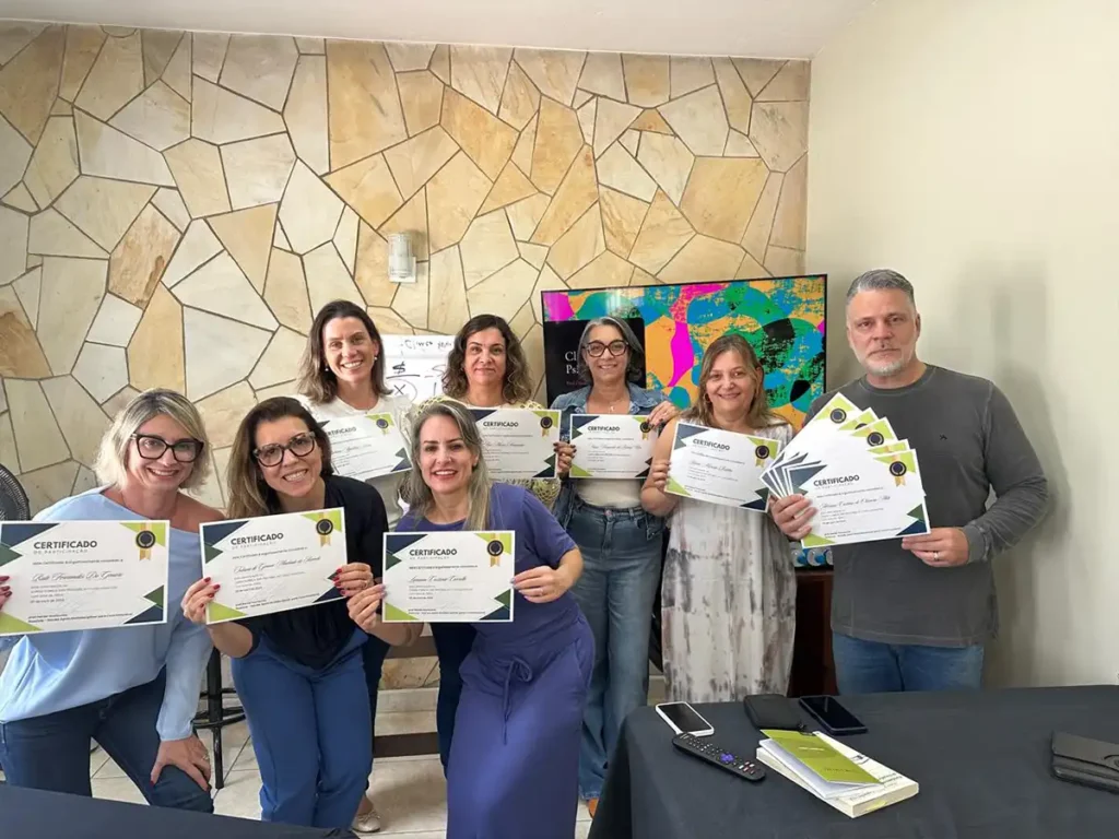 Grupo de psicólogos e terapeutas celebrando com certificados após conclusão de treinamento em sala locada para profissionais da saúde mental em Campinas.